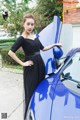 A woman in a black dress standing next to a blue car.