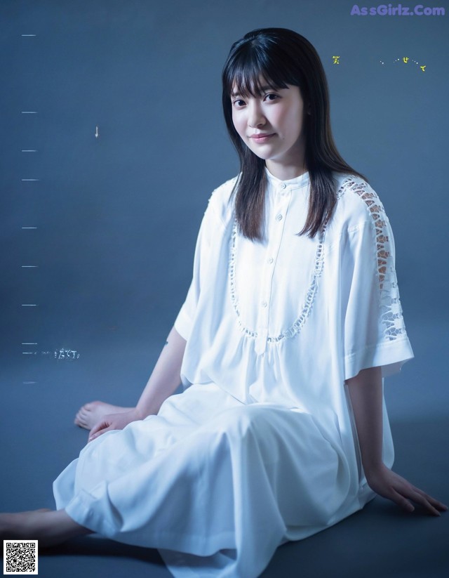 A woman in a white dress sitting on the ground.