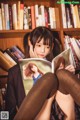 A woman sitting in front of a bookshelf reading a book.