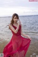 A woman in a red dress standing on a beach.