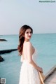 A woman in a white dress standing on a pier by the ocean.